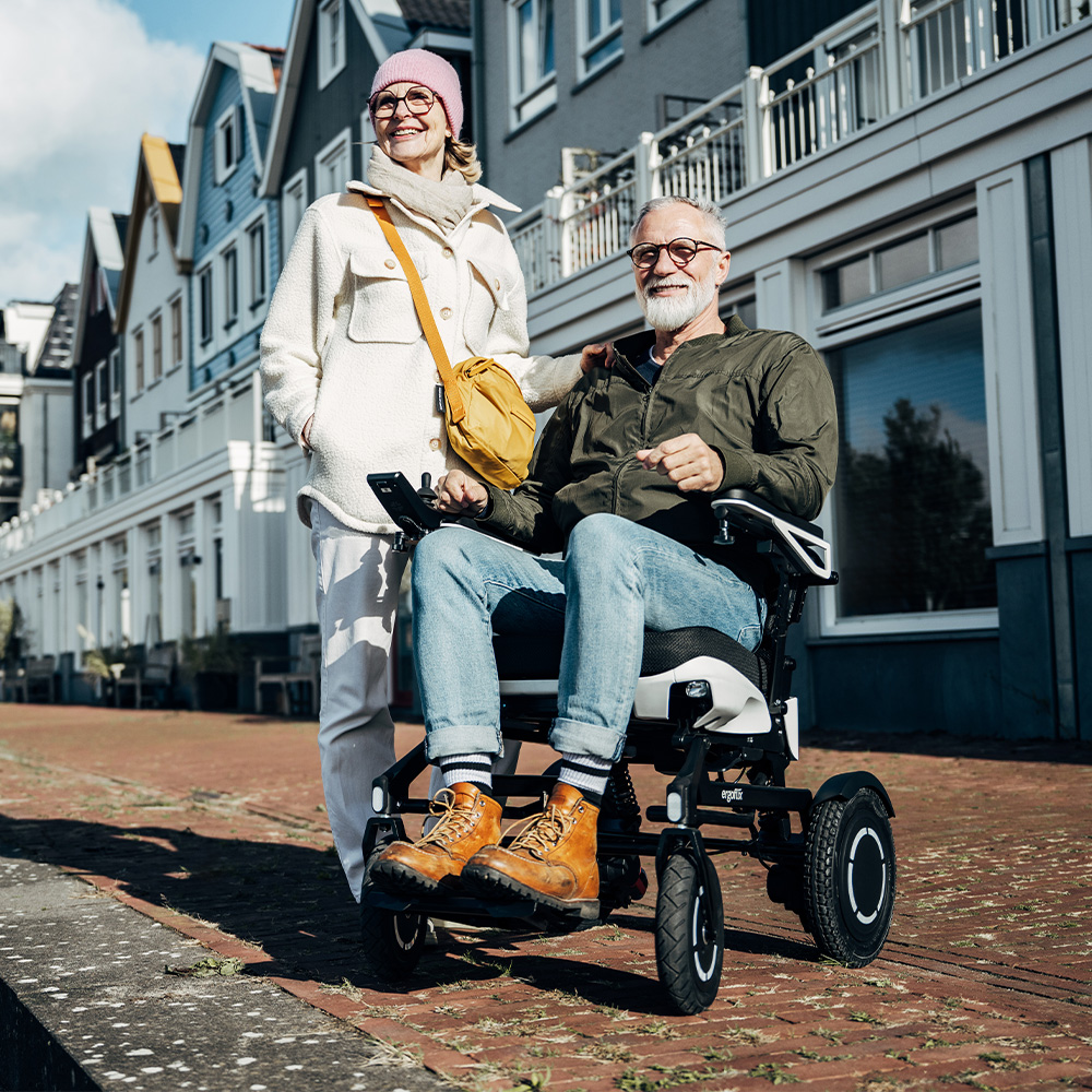 Un señor mayor sentado en una silla de ruedas ergoflix® vario mira a lo lejos junto a una señora mayor.